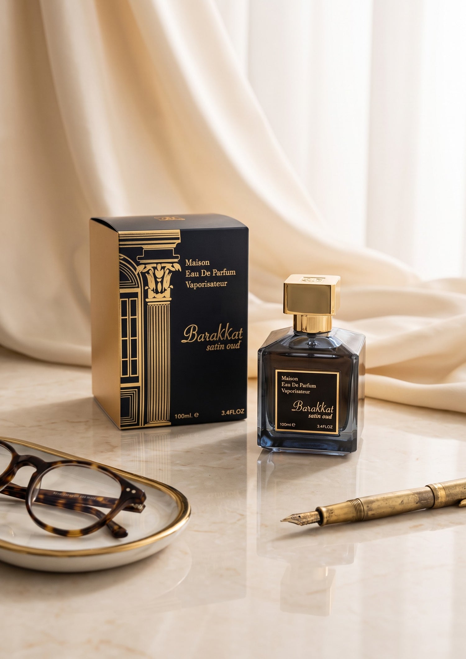 Flacon et boîte de parfum PDS SHOP Barakkat Satin Oud sur une table en marbre avec des lunettes et un stylo plume.
