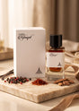 Flacon de parfum PDS SHOP Rifaaqat 85ml avec sa boîte blanche, entouré de grains de poivre, safran et copeaux de bois